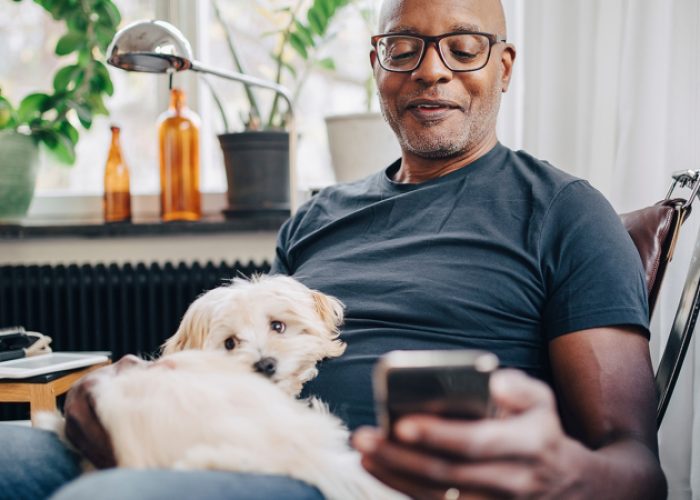 Smiling retired senior male using smart phone while sitting with dog in room at home

Credit: Getty